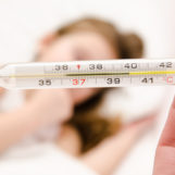 Mother holding thermometer foreground and sick little girl Mother holding thermometer foreground and sick little girl in bed